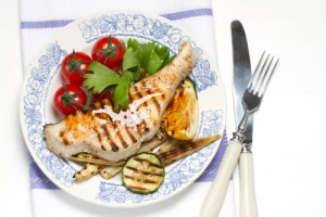 An image of grilled swordfish on a plate with tomatoes and greens.