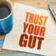 An image of a cup of coffee beside a napkin with block letters that read trust your gut.