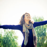 An image of an attractive woman with outstretched hands standing outdoors.