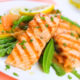 An image of grilled salmon with spring vegetables on white plate.