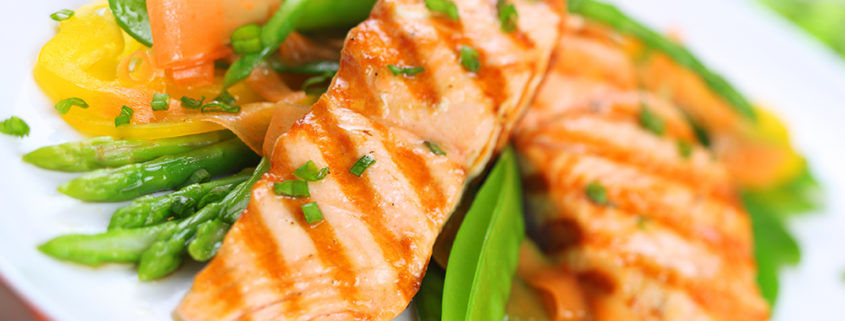 An image of grilled salmon with spring vegetables on white plate.