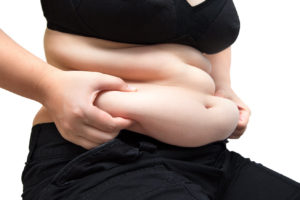 An image of an overweight woman in exercise clothes pinching her fat belly with her fingers. 