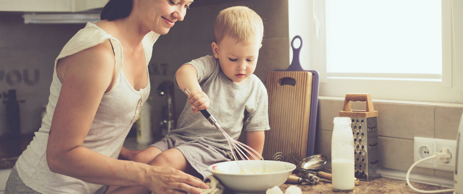 An image of a mother and her two-year-old so cooking in the kitchen. 