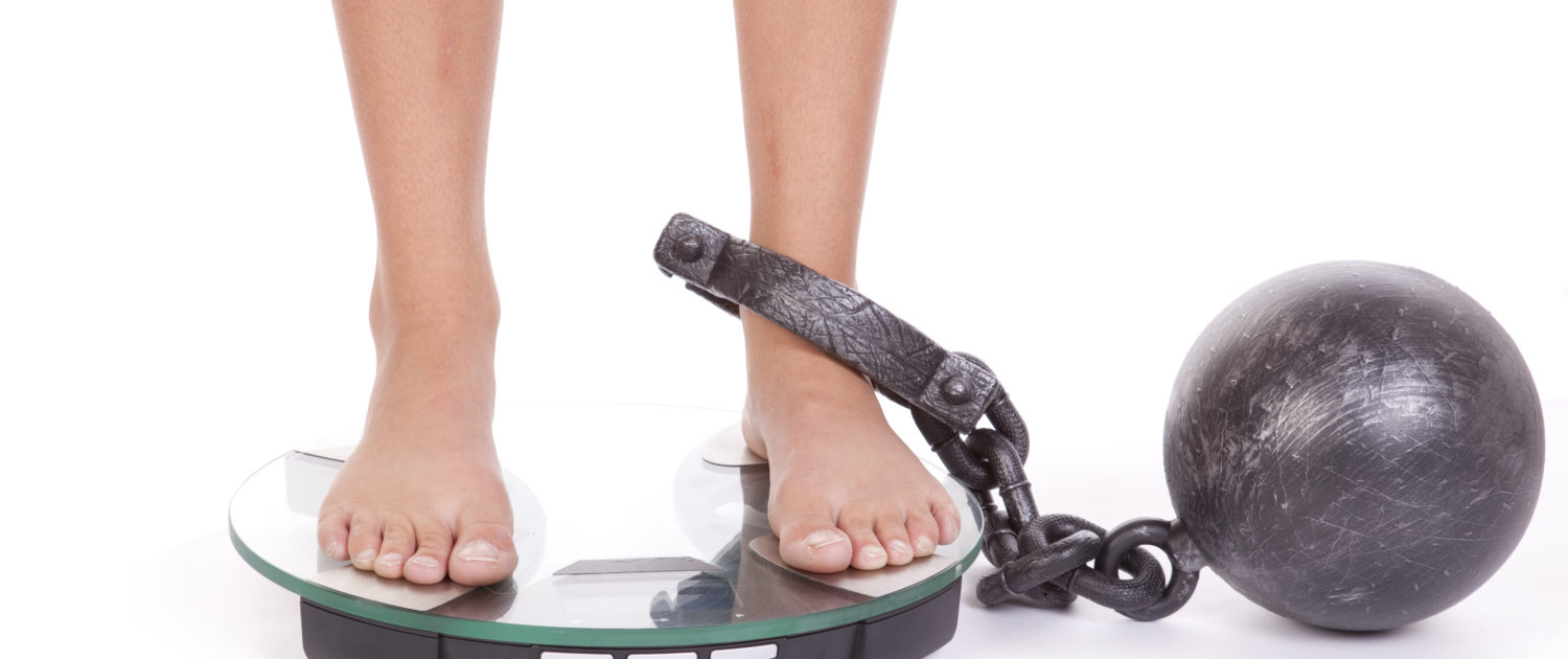 An image of feet on a weight scale with a ball-and-chain attached to her ankle.