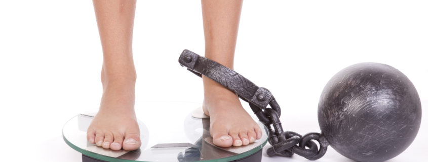 An image of feet on a weight scale with a ball-and-chain attached to her ankle.