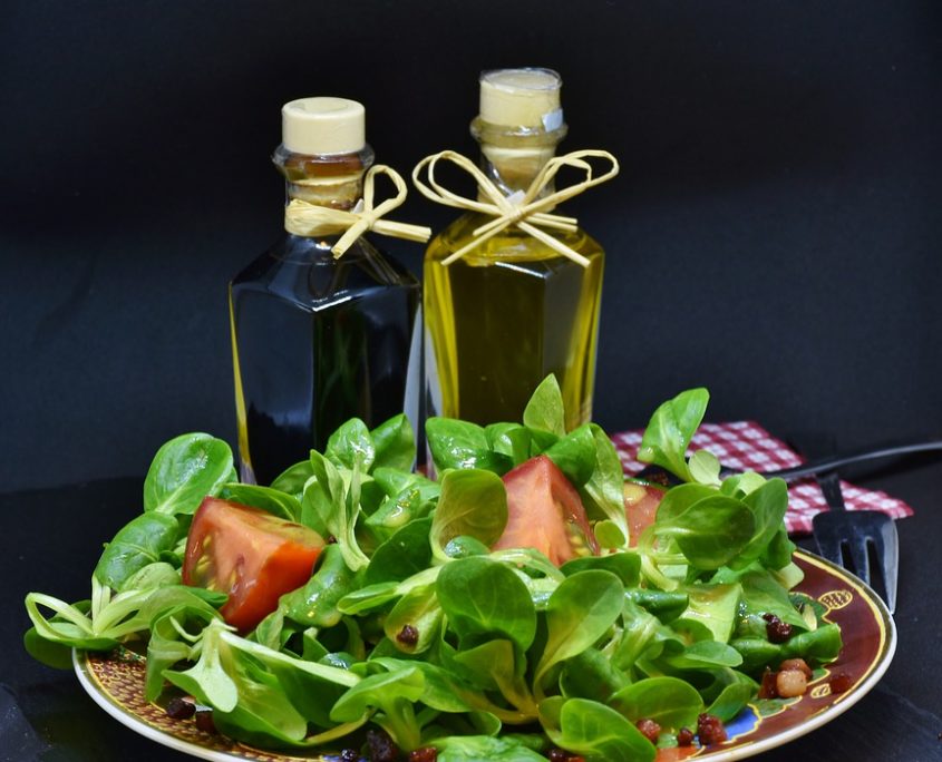 An image of a salad on a plate in front of oil and vinegar bottles. 