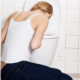 An image of a young woman on her knees throwing up in a toilet.