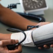 An image of a man's hands taking a patient's blood pressure with a cuff.