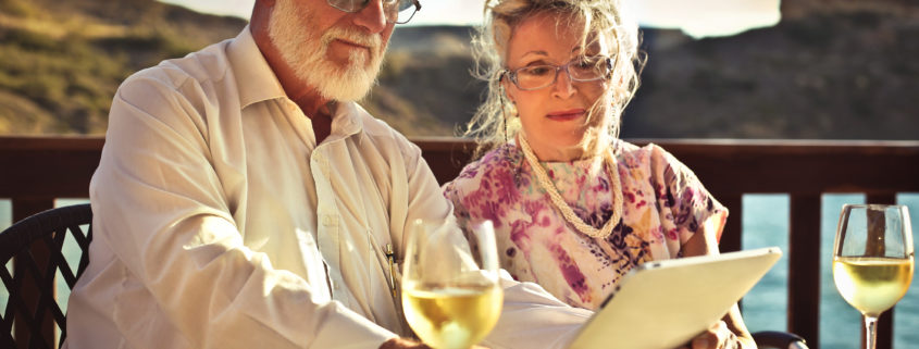 An image of a husband and wife sitting at a table on a deck with a glass of wine.