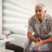 An image of a senior male sitting on the edge of his bed.