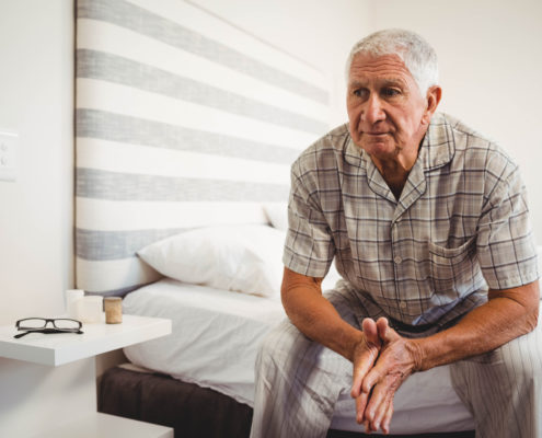 An image of a senior male sitting on the edge of his bed.