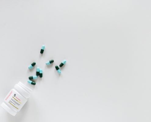 An image of prescription capsules spilled out of the bottle on a white background.