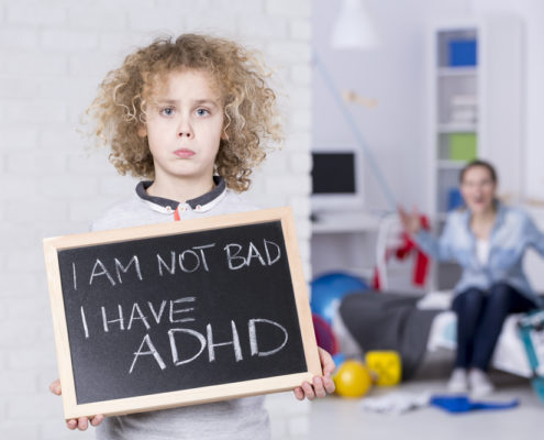 An image of a sad boy holding a small chalkboard that reads, "I am not bad. I have ADHD". Shouting mother is in background.