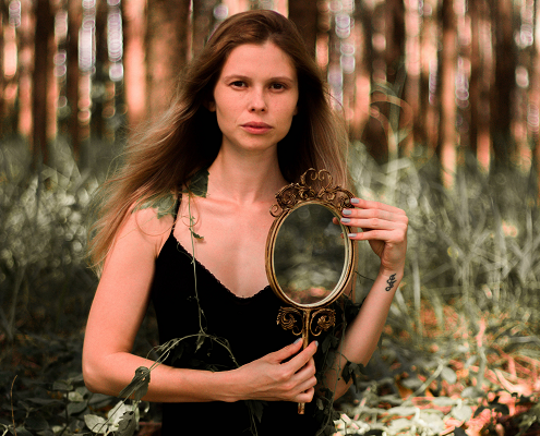 An image of an attractive woman in the forest holding a hand mirror. 