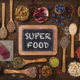 An image of several wooden scoops with various superfoods, like pomegranate and nuts, surrounding a chalkboard sign that reads super food.