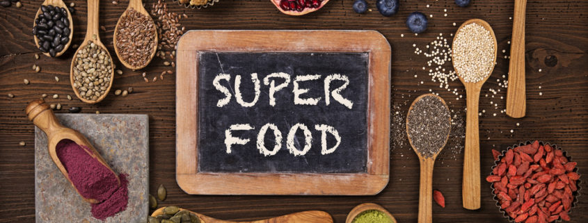 An image of several wooden scoops with various superfoods, like pomegranate and nuts, surrounding a chalkboard sign that reads super food.