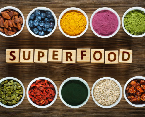 An image of several bowls of superfoods, including blueberries, turmeric, and seeds surrounding wood blocks that read superfood.