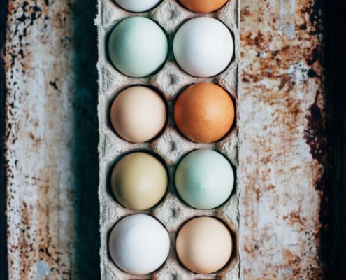 An image of an open carton of different colored chicken eggs.