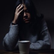 An image of an anxious woman holding her head in her hand in a dark room.