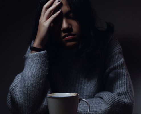 An image of an anxious woman holding her head in her hand in a dark room.