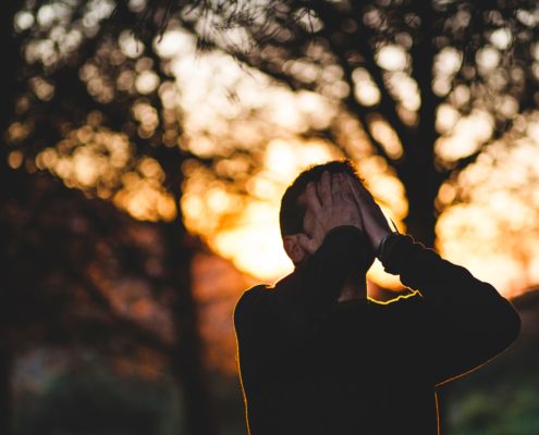 An image of a man covering his face with his hands with sunset.