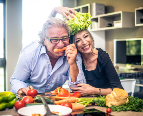 An image of a mature couple sitting at a table with healthy food, like tomatoes, bell peppers, and lettuce.