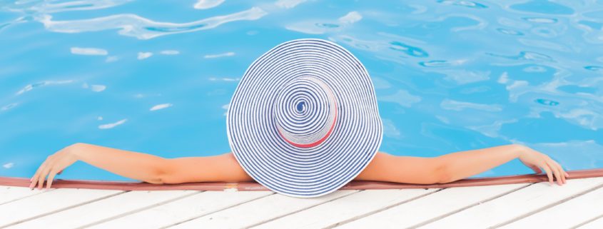An image of a woman in a floppy hat lounging in a swimming pool, her arms on the deck behind her.
