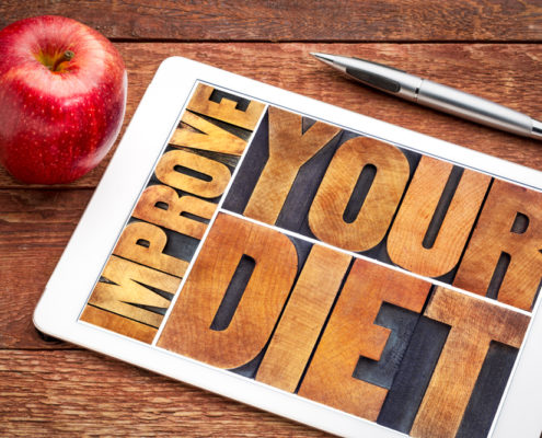 An image of an apple and an ink pen on a table beside a wooden-lettered sign that reads improve your diet. 