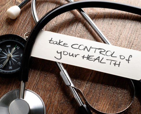 An image of a stethoscope and compass on a wood table with a hand-written sign that reads take control of your health.
