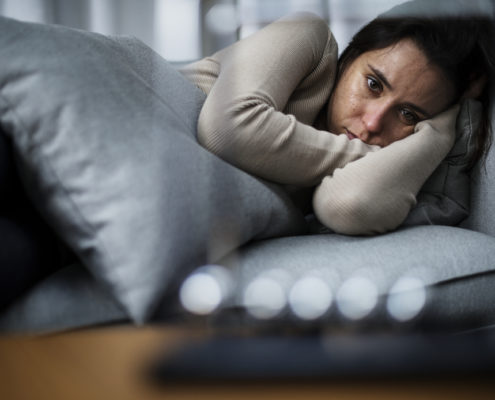 An image of a depressed woman lying on her side in bed. 