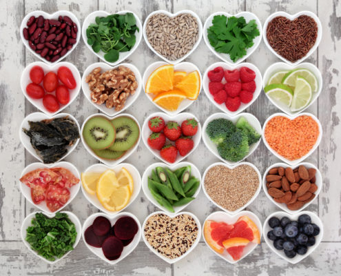 An image of a collection of heart-shaped bowls filled with a variety of superfoods on wooden background.