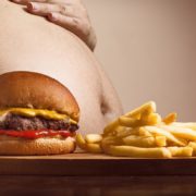An image of a man's bare fat belly beside a table of fries and a hamburger sandwich.