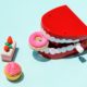 A cartoon image of toy false teeth, a donut, piece of cake, and a cupcake on blue background.