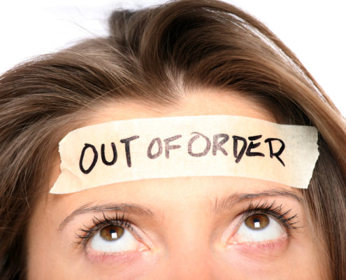 An image of a woman's face with masking tape on her forehead with text that reads: out of order.