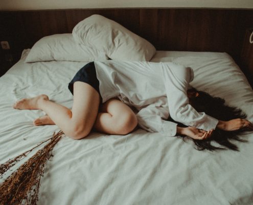 An image of a fully clothed woman curled up in bed.