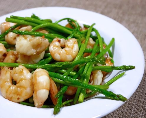 An image broiled shrimp and asparagus in a white bowl.