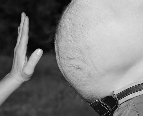 An image of a woman's hands starting to touch a man's big bulging bare belly.