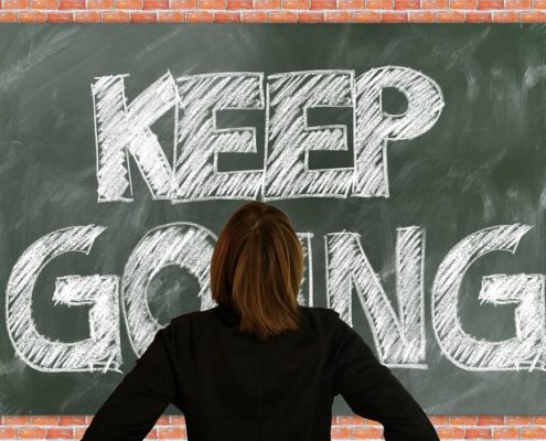 An image of a woman staring at large chalkboard with text that reads "keep going."