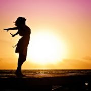 A silhouette of a woman standing on a beach at sunrise, hands thrown back in joy.