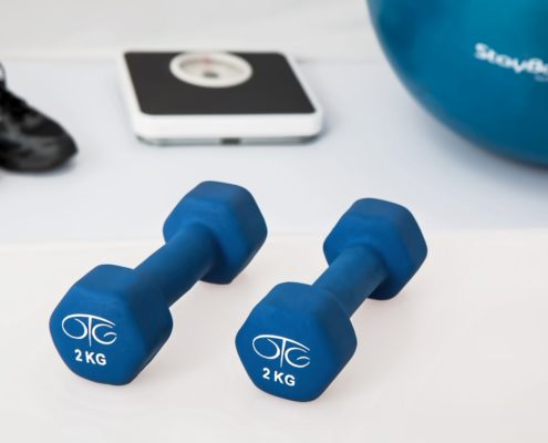 An image of a bathroom scale, black athletic shoe, two blue dumbbells, and a blue stability ball on a white background.