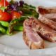 An image of sliced pork, asparagus, and tomatoes on a white plate.