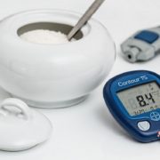 An image of a glucose monitor and a bowl of sugar on a white background.