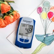 An image of a glucose monitor, flowers, and a picture of a girl with balloons on a table.