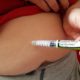 An image of an obese man inserting a syringe of insulin into his belly.