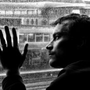 An image of a depressed man looking through the window at the rain.