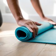 An image of a woman rolling up a yoga mat on the floor.