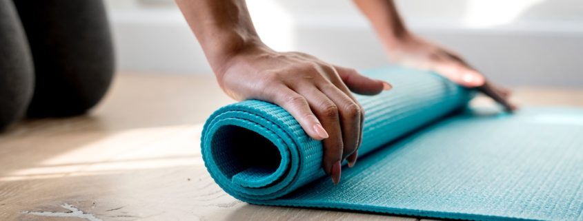 An image of a woman rolling up a yoga mat on the floor.