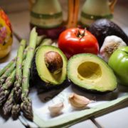 An image of a tray with asparagus, garlic cloves, avocado halves, and tomatoes on a table.