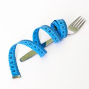 An image of a tape measure encircling a fork on light gray background.