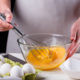 A cropped image of a woman hand mixing eggs with a whisk in a glass bowl.